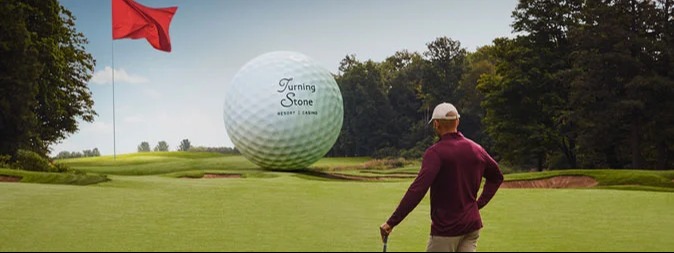 A guy on the golf course with a giant turning stone golf ball