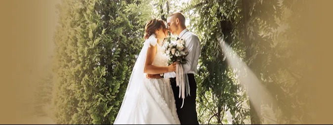 A bride holding a bouquet while embracing her groom between evergreen trees